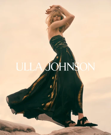 Model wearing a black and gold dress posing on a rocky outcrop against a pale sky