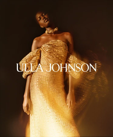 Model wearing a textured gold strapless gown with sculptural drop sleeves and a matching statement collar against a dark background.