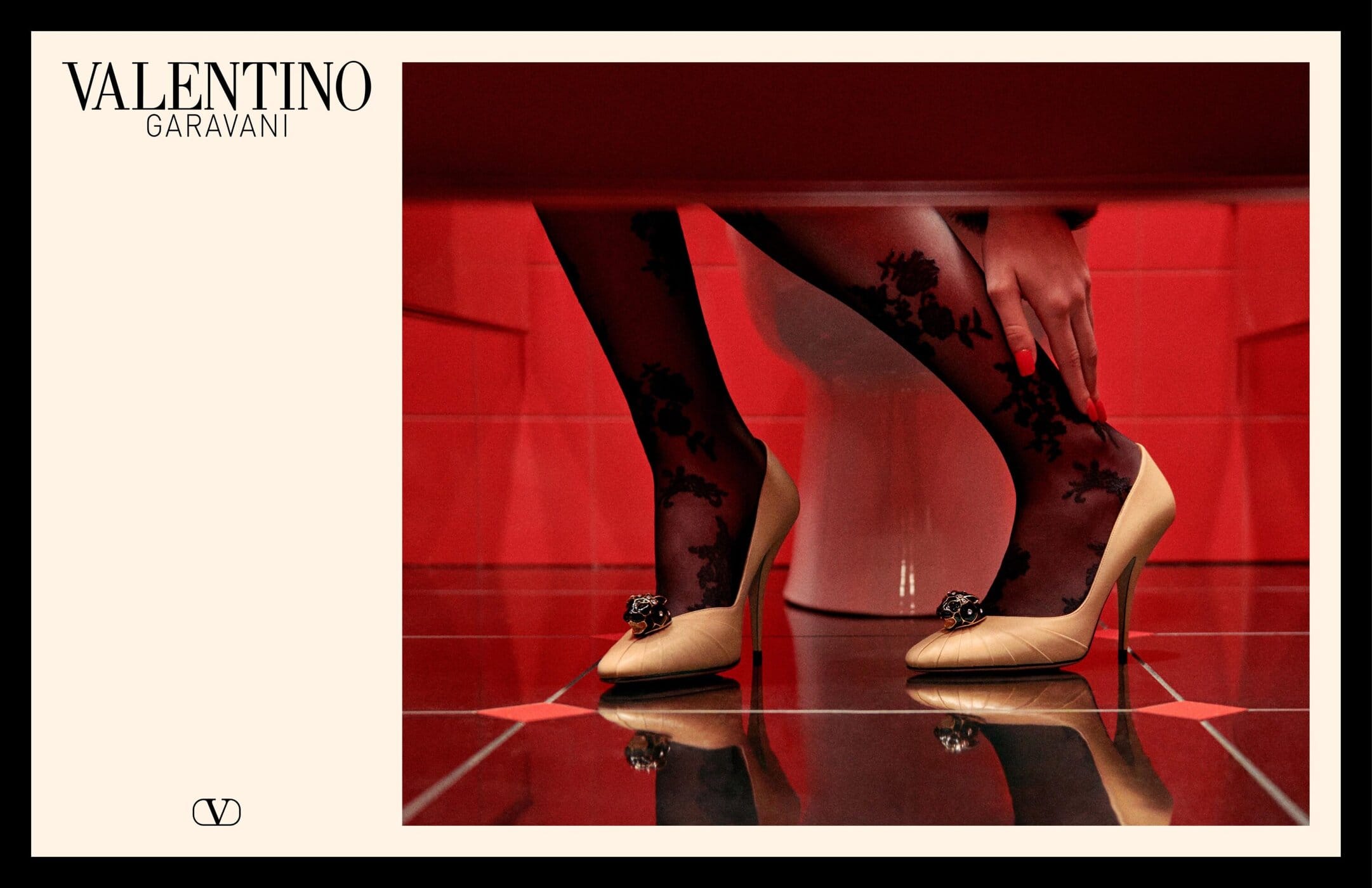 Close-up of legs in black floral patterned tights and cream high heels against a red tiled wall background.
