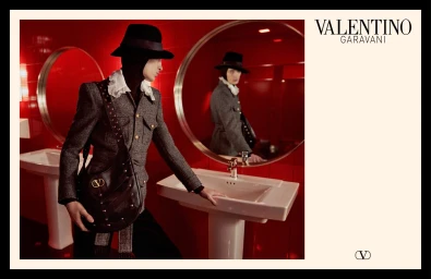 Model in tweed jacket and hat holding studded leather handbag in red tiled washroom with round mirror for Valentino campaign