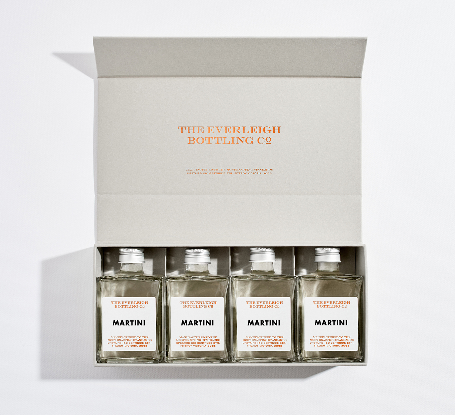 An open grey presentation box holding four bottled martini cocktails by The Everleigh Bottling Co on a white background