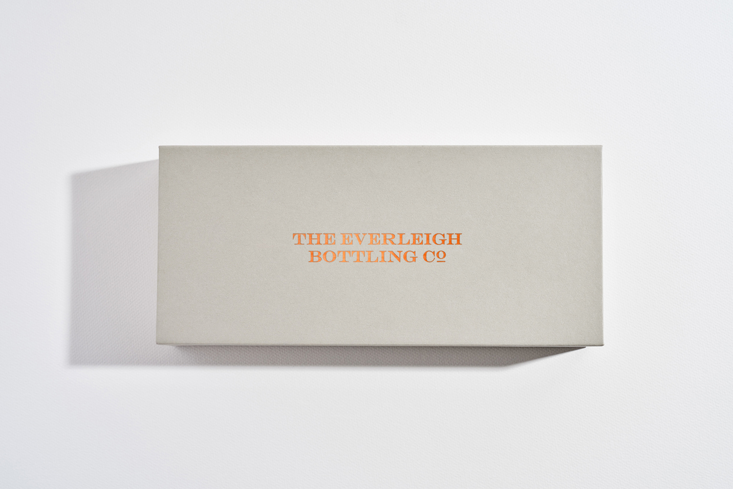 Rectangular grey rigid box with metallic copper foil lettering against a white seamless background