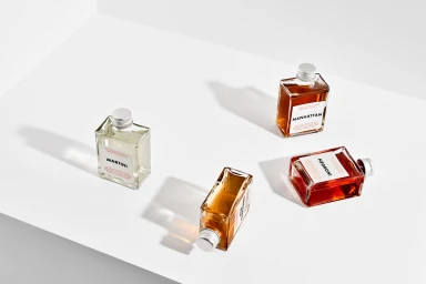 Four square glass bottles of cocktail beverages arranged on a plain white surface with crisp shadows.