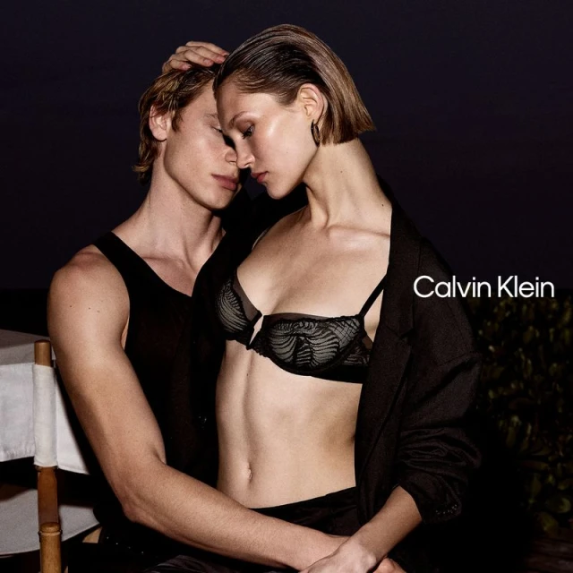 A captivating Calvin Klein ad featuring a blonde couple embracing intimately, the woman in black lingerie, set against a dark backdrop.