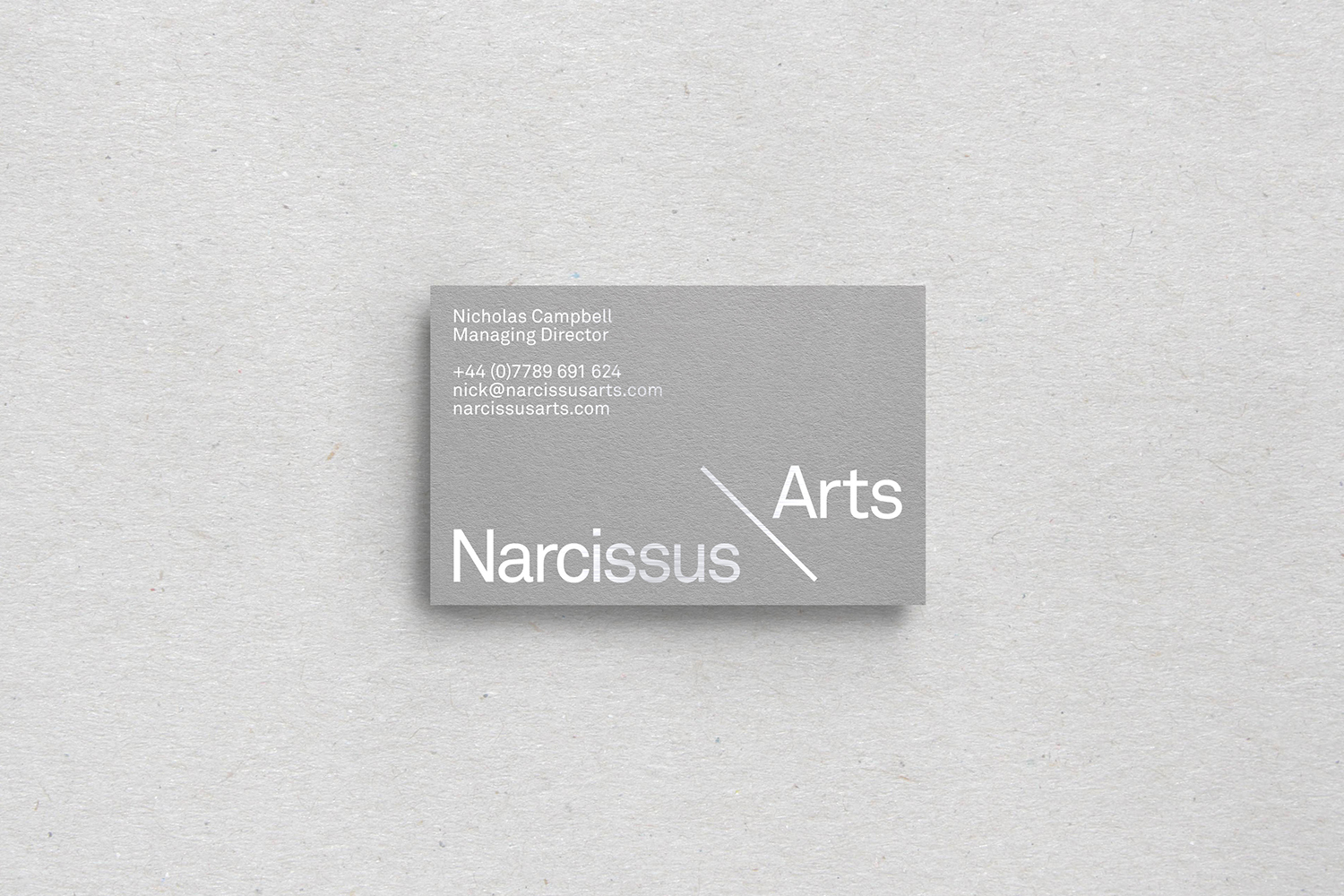 Grey business card with clean white typography resting on a textured light grey paper background
