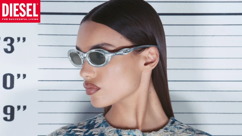 Model wearing silver futuristic sunglasses and textured denim top against a police lineup background for Diesel