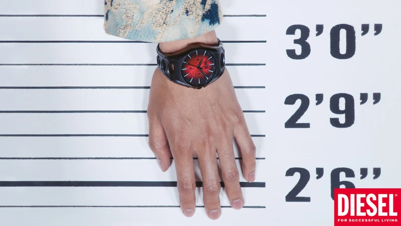Close-up of a person wearing a black and red Diesel watch against a height chart backdrop for Diesel Fall 2025.