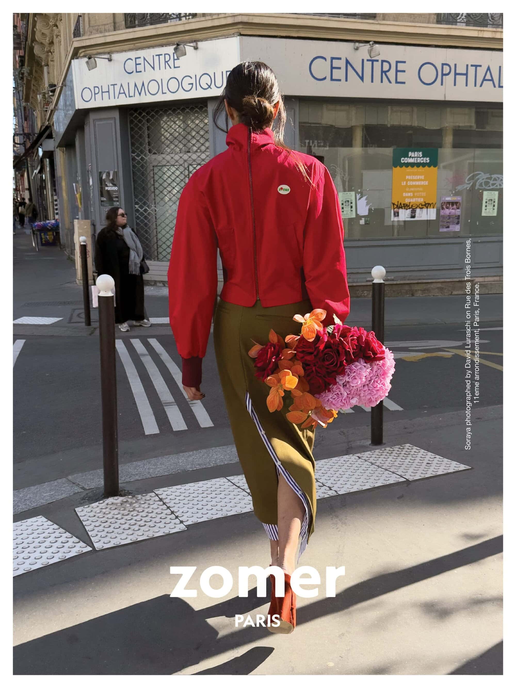 Model walking away on a city street carrying a bouquet of colorful red, orange, and pink flowers