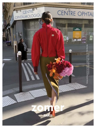 Model walking away on a city street carrying a bouquet of colorful red, orange, and pink flowers