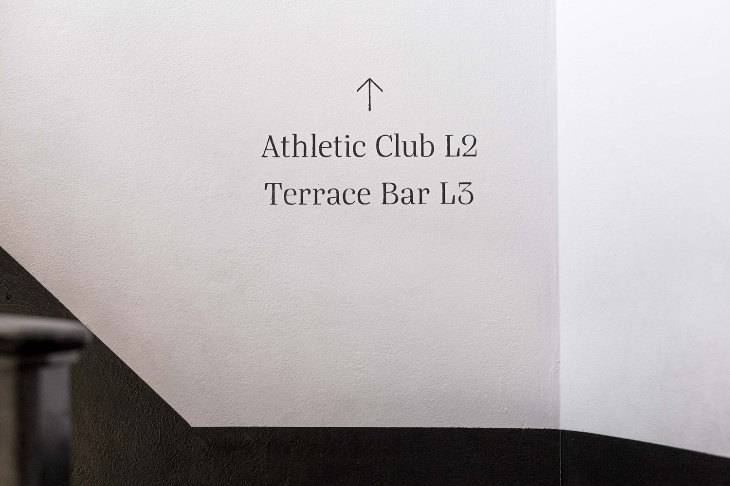 Minimalist directional signage on a white wall pointing to Athletic Club L2 and Terrace Bar L3 for East Village Sydney