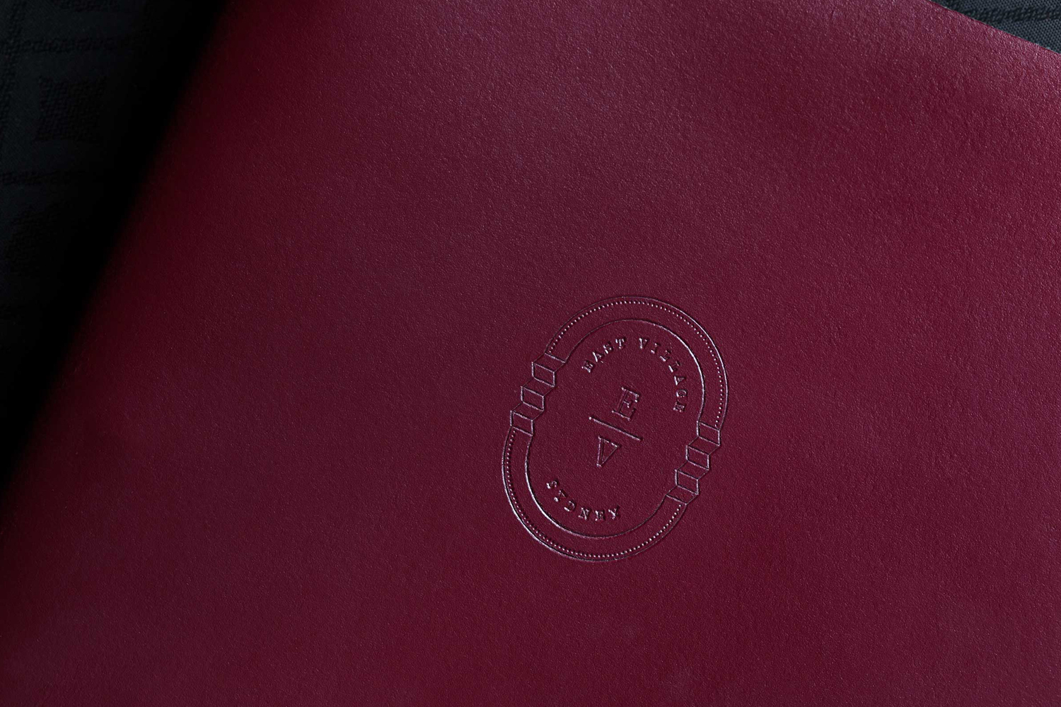 Embossed silver logo on dark burgundy textured paper for the East Village Sydney brand identity project by The Colour Club.