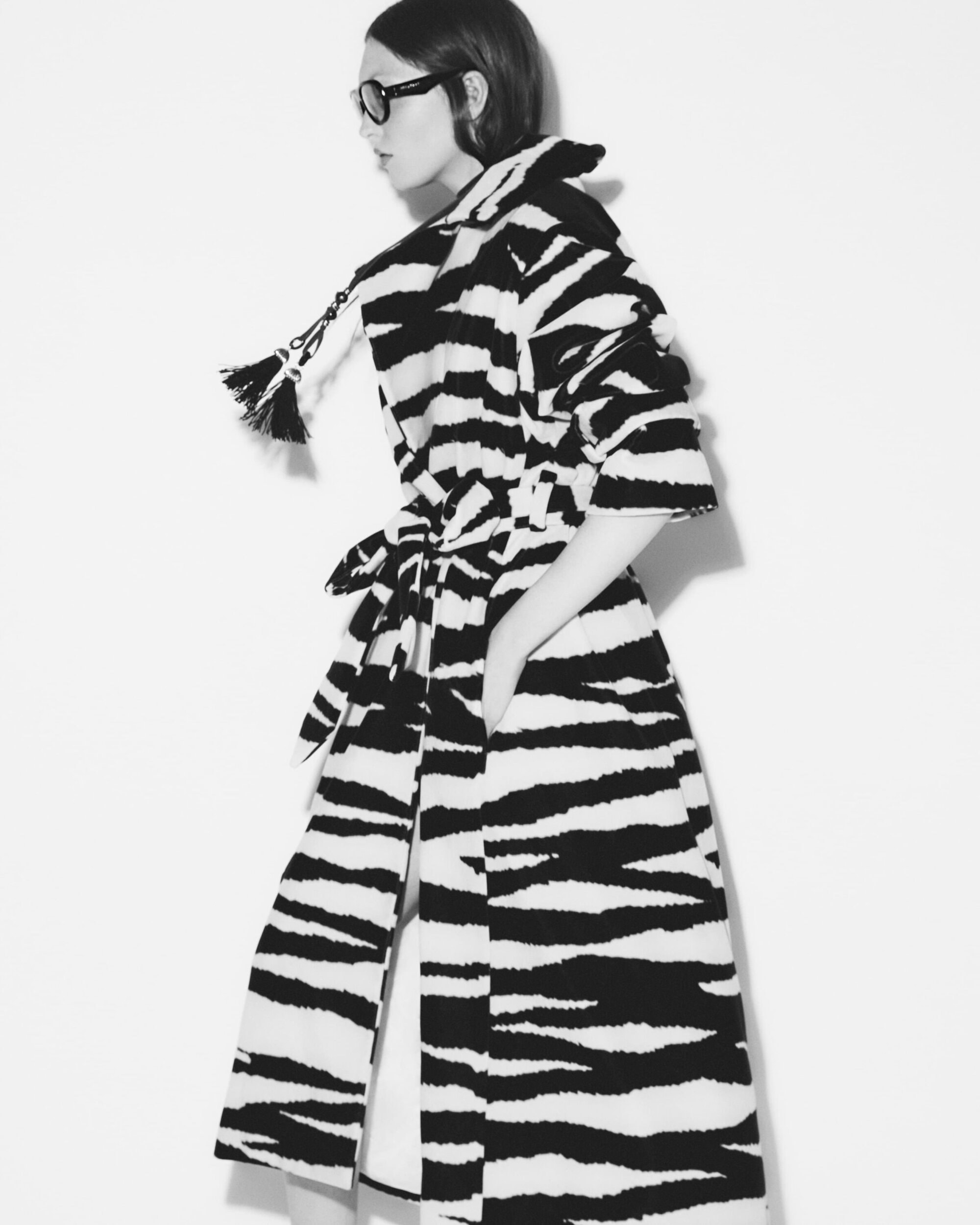 Model in black-and-white zebra print belted coat wearing dark sunglasses against a plain white background