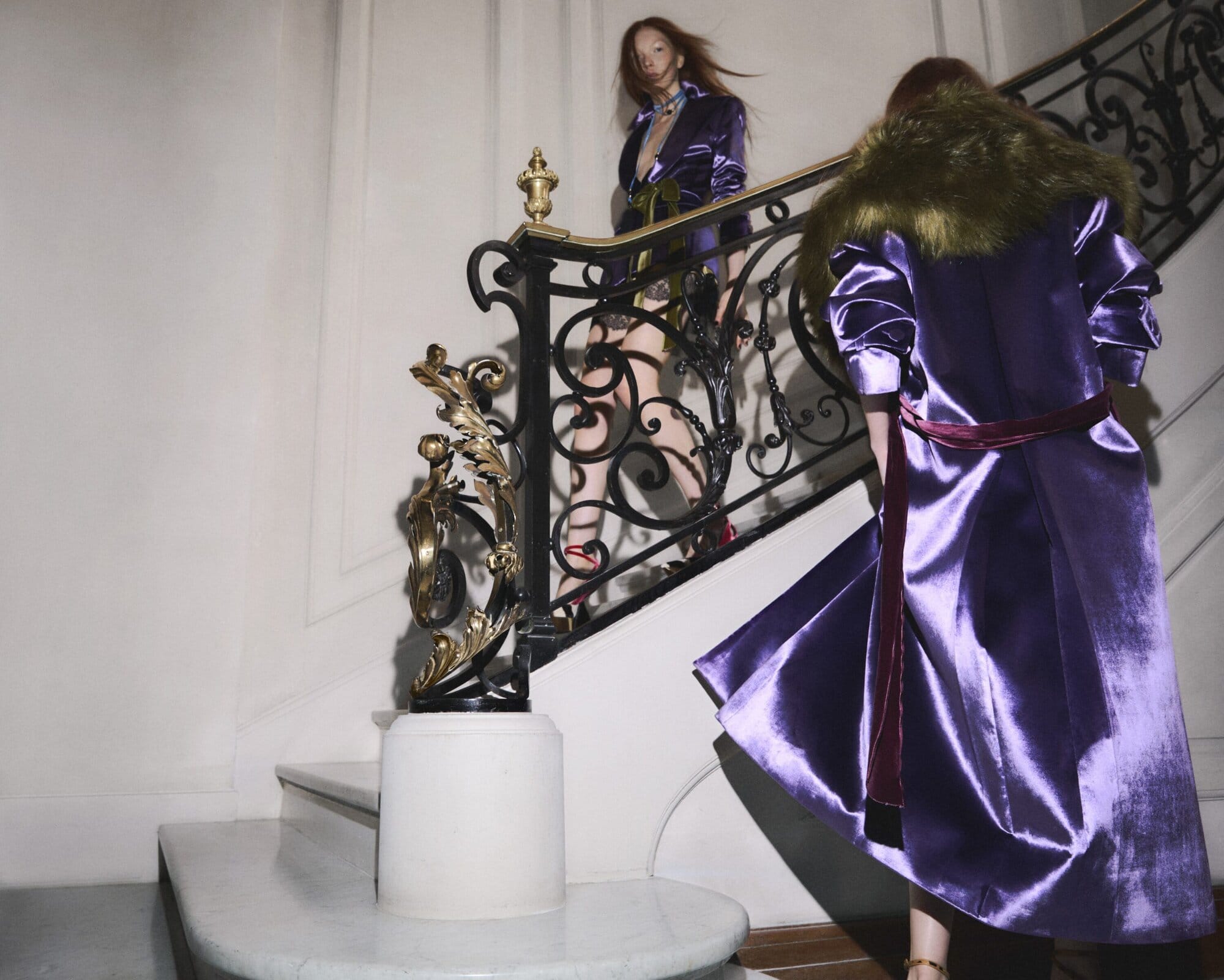Two models descending a grand staircase in vibrant purple satin coats during the Nina Ricci Fall 2025 ad campaign.