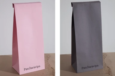 Two tall paper bags in light pink and dark grey with brand text standing on a textured neutral surface.