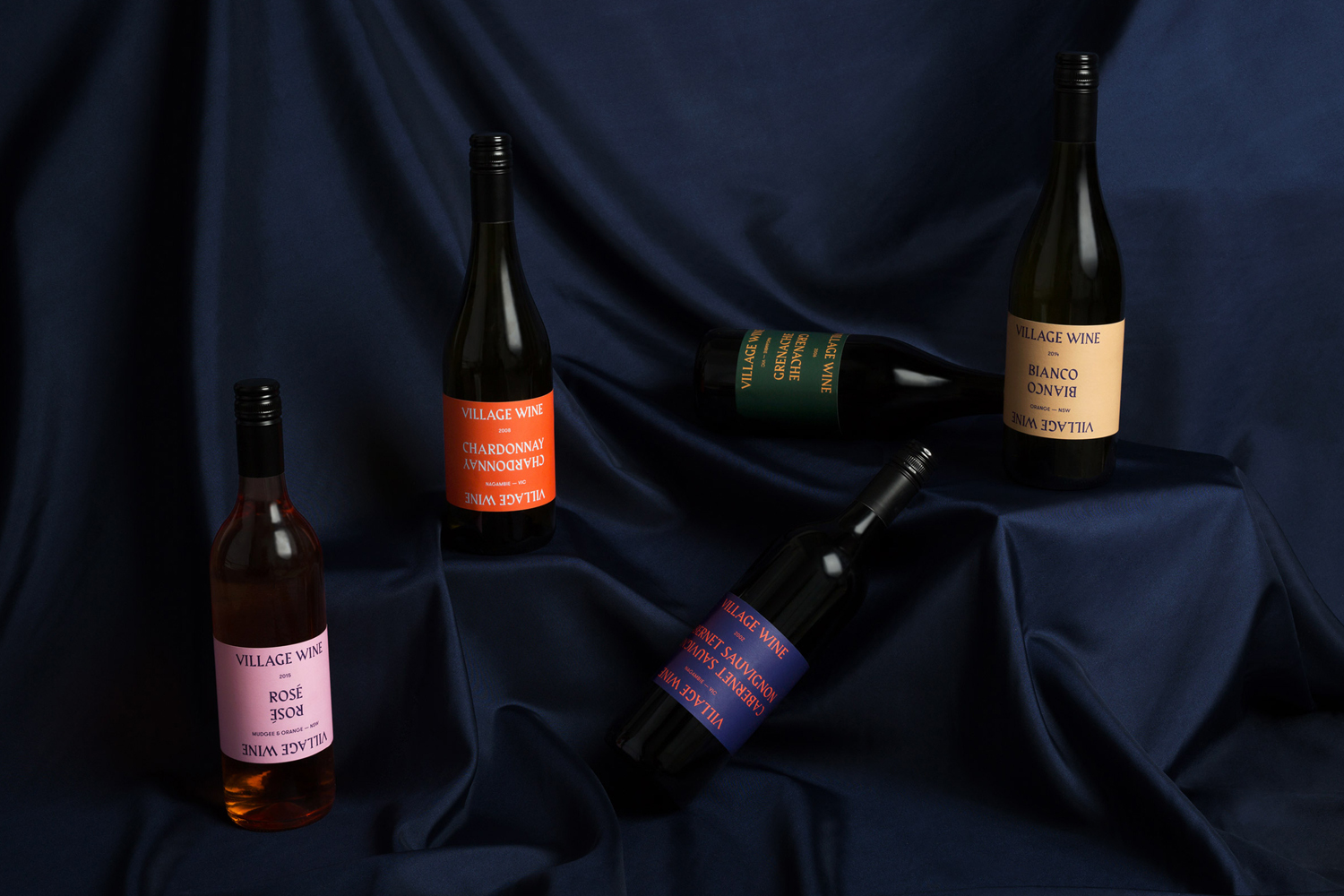Five wine bottles with colorful labels arranged on a draped dark blue fabric backdrop