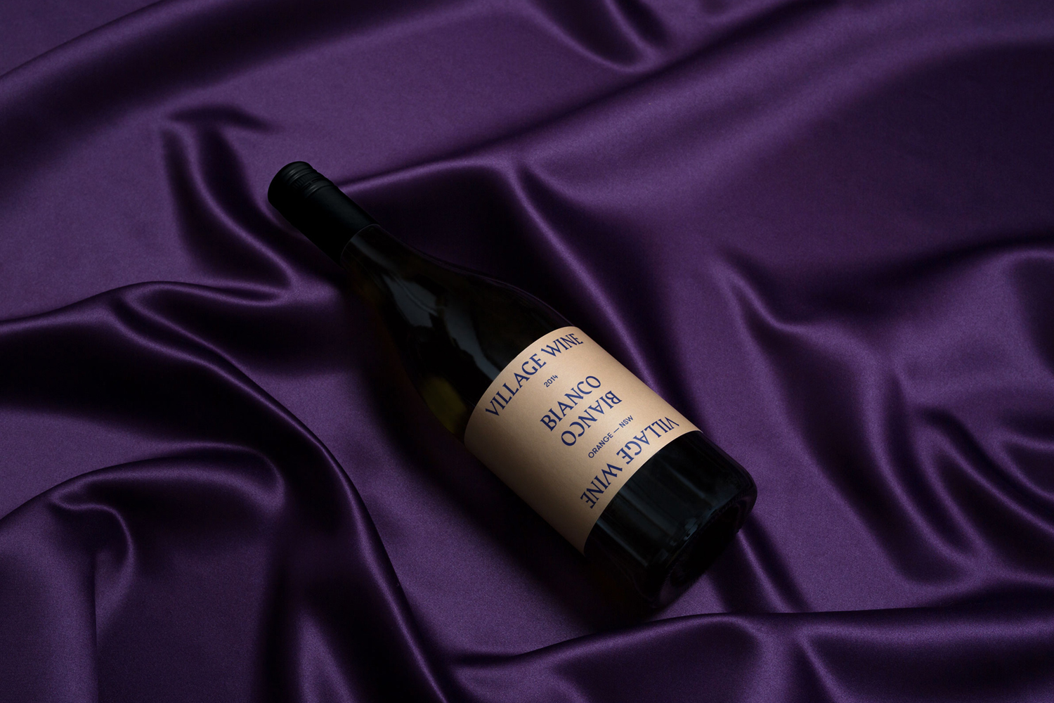 A wine bottle resting diagonally on a deep purple satin fabric background with soft folds.