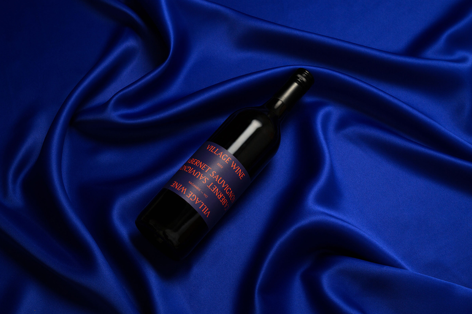 Wine bottle resting diagonally on draped royal blue fabric with visible folds