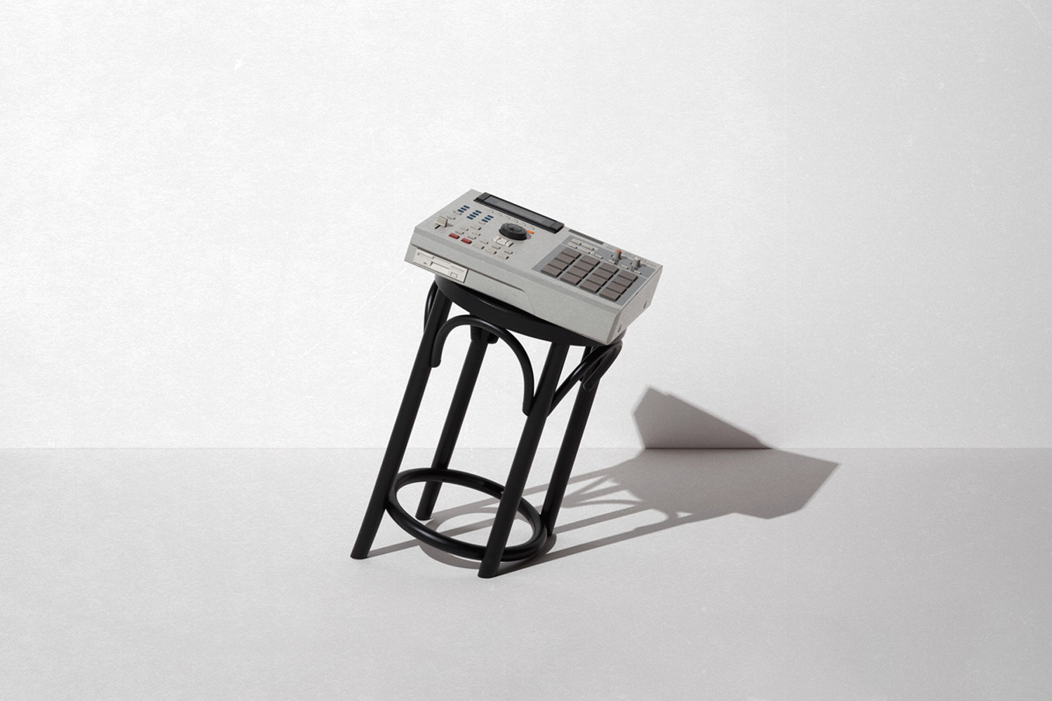 Vintage grey music sampler resting diagonally on a black wooden stool against a neutral white wall.