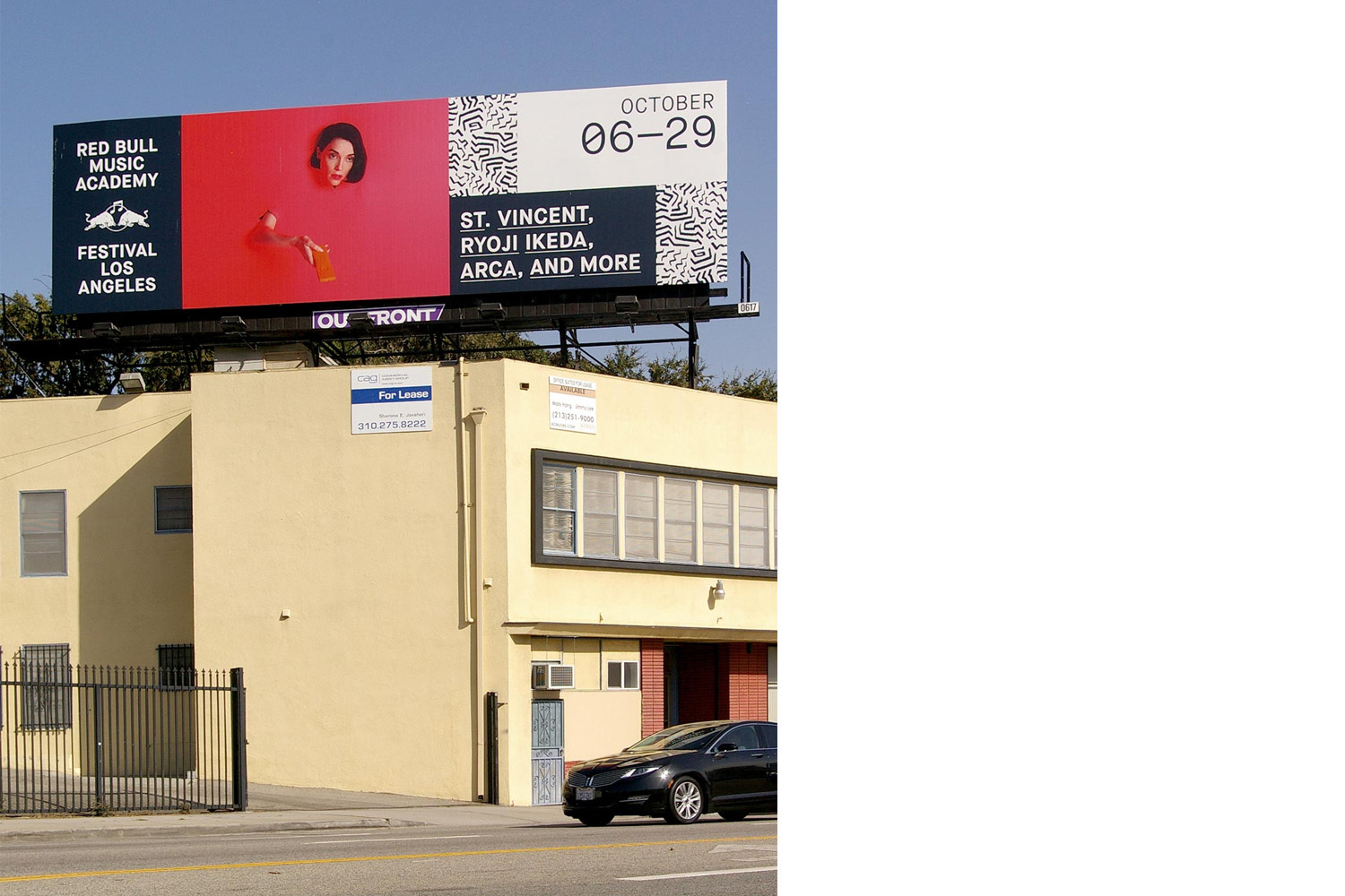 Large Red Bull Music Academy billboard mounted above a cream commercial building with a black car parked in front.