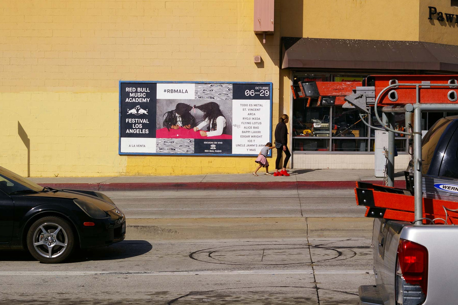 Red Bull Music Academy billboard on a yellow building exterior with pedestrians walking along the sidewalk.