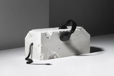 Black over-ear headphones resting on a textured white rectangular stone block with a coiled audio cable extending out.