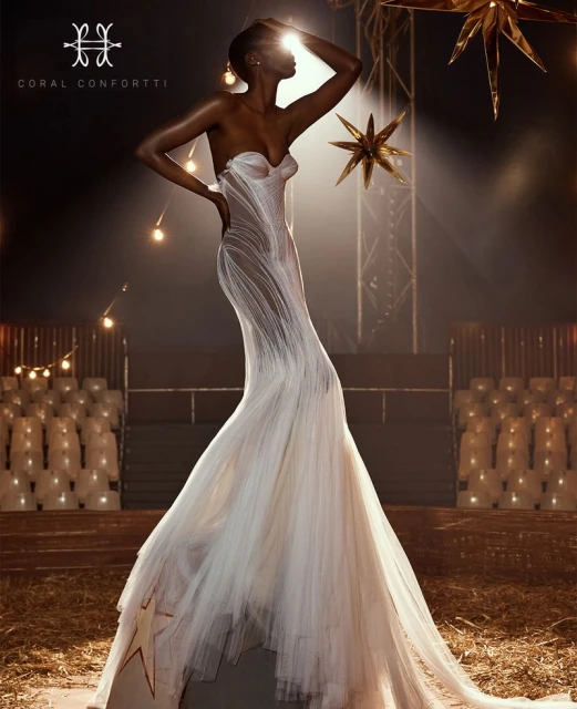 Elegant dark-skinned woman in a white strapless gown posing in a dimly lit space with string lights and star decorations.