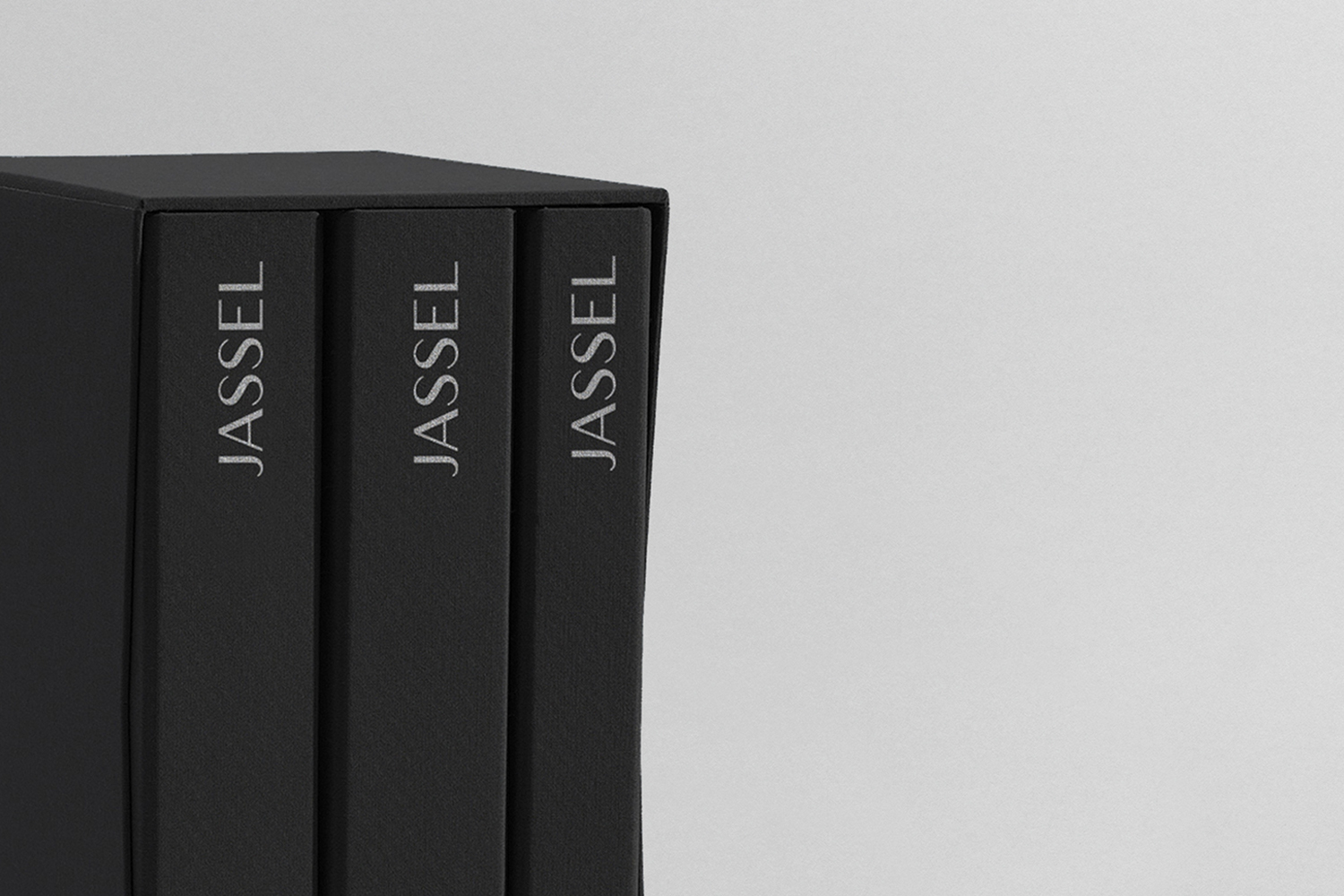 Three black boxed books with white typography reading Jassel against a pale grey studio seamless background