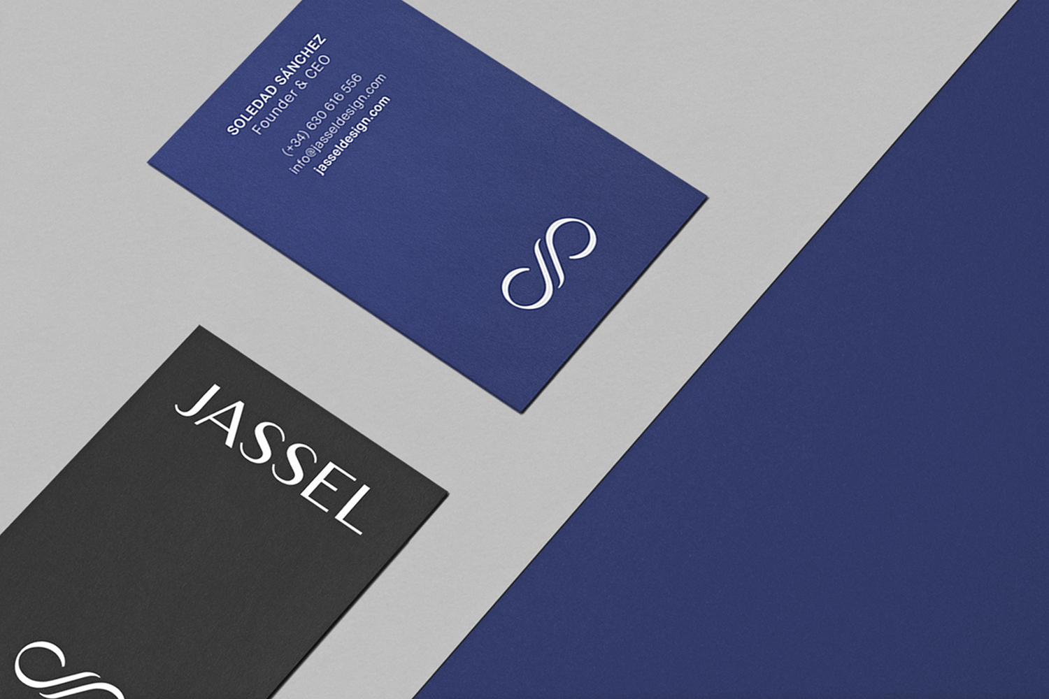 Business cards for Jassel featuring a blue card with white text and logo alongside a black card on a grey textured surface.