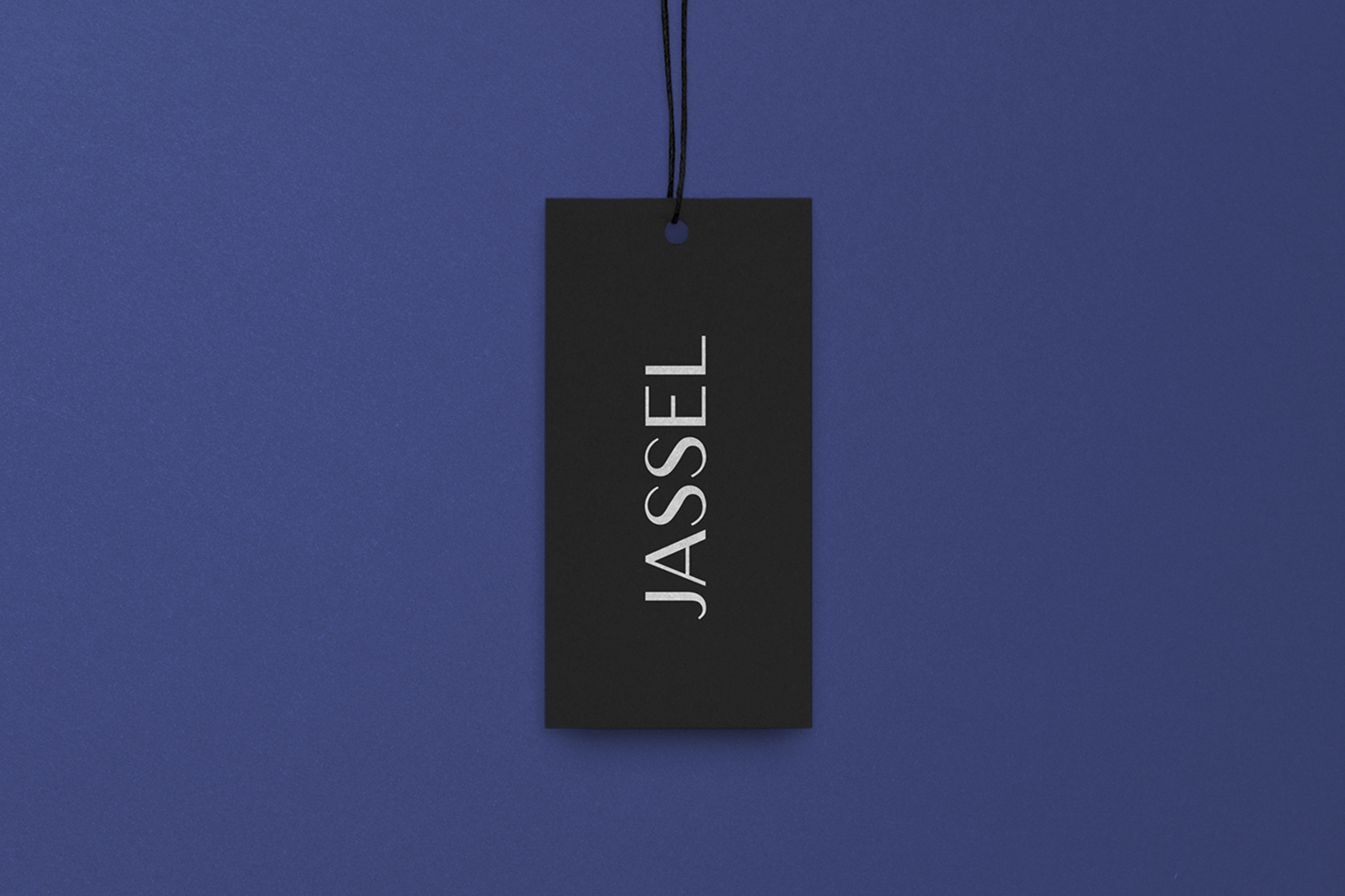 Black clothing tag with white text reading Jassel suspended by a black string against a textured blue background