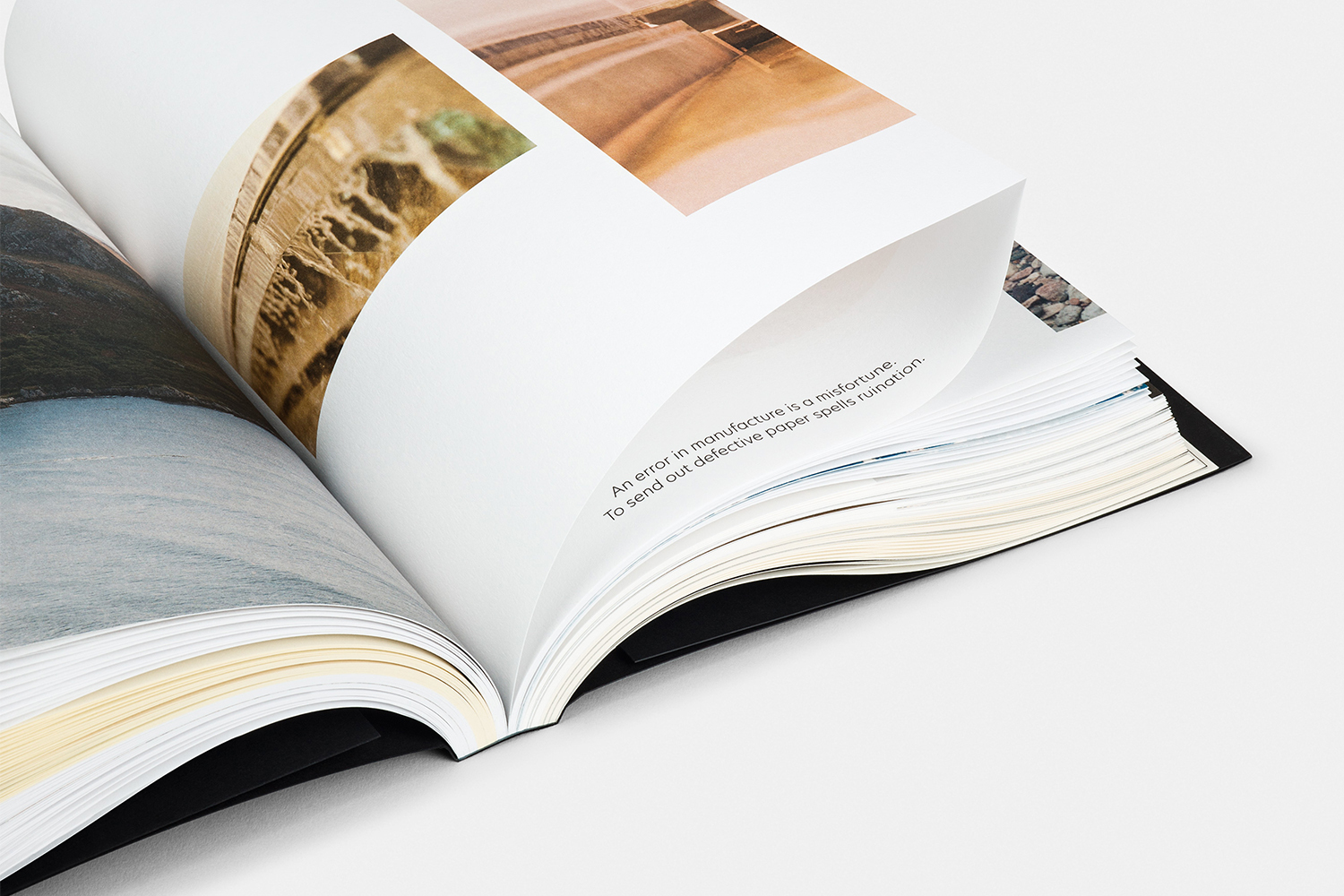 An open book with pages curling over, displaying landscape photography and printed typography against a plain white background.