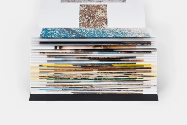 Close-up of a stacked book pages edge showing colorful printed imagery and paper textures on a neutral background.