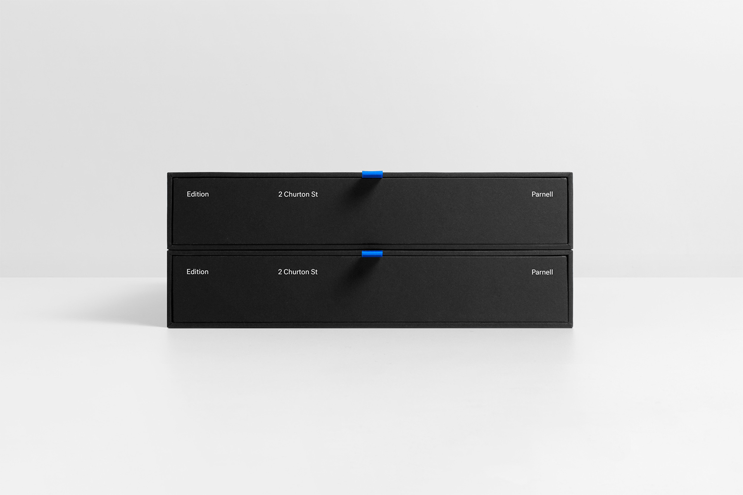 Two stacked black rectangular presentation boxes with white typography and small blue pull tabs on a white surface