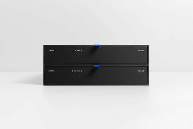 Two stacked black rectangular presentation boxes with white typography and small blue pull tabs on a white surface