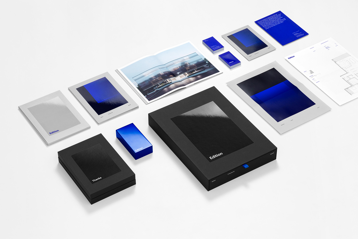 An elevated view of a branding identity set including black presentation boxes, printed stationery, and booklets featuring blue graphic accents on white.