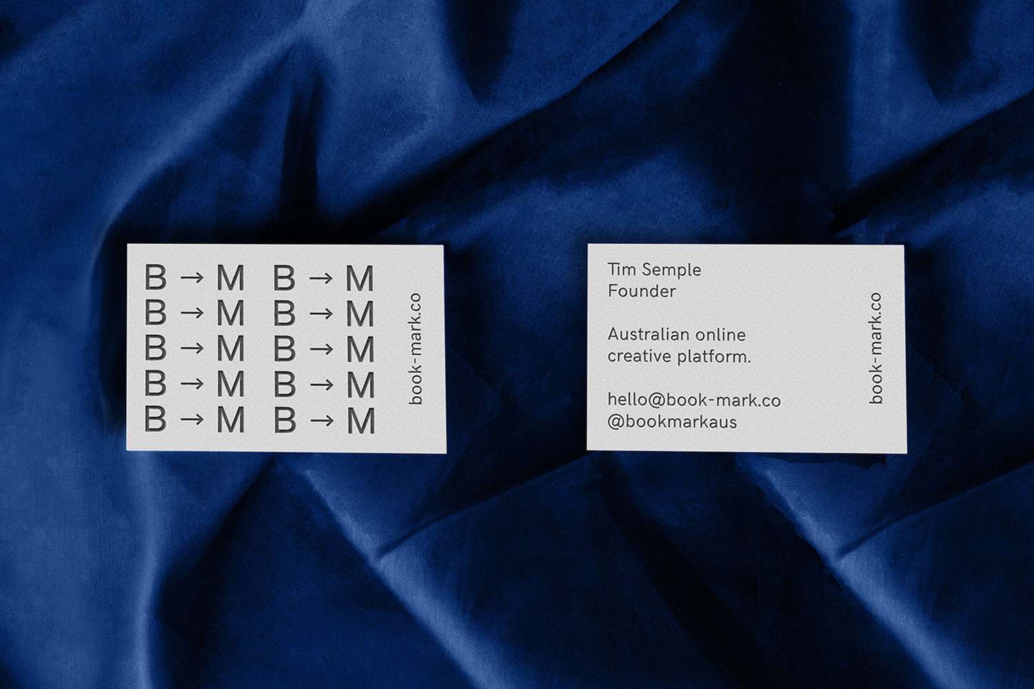 Two white business cards resting on a textured dark blue velvet fabric background, showcasing minimalist typography and branding.