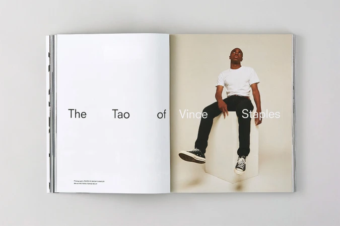 An open magazine spread featuring typography on the left page and a portrait of a man seated on a white cube on the right page.