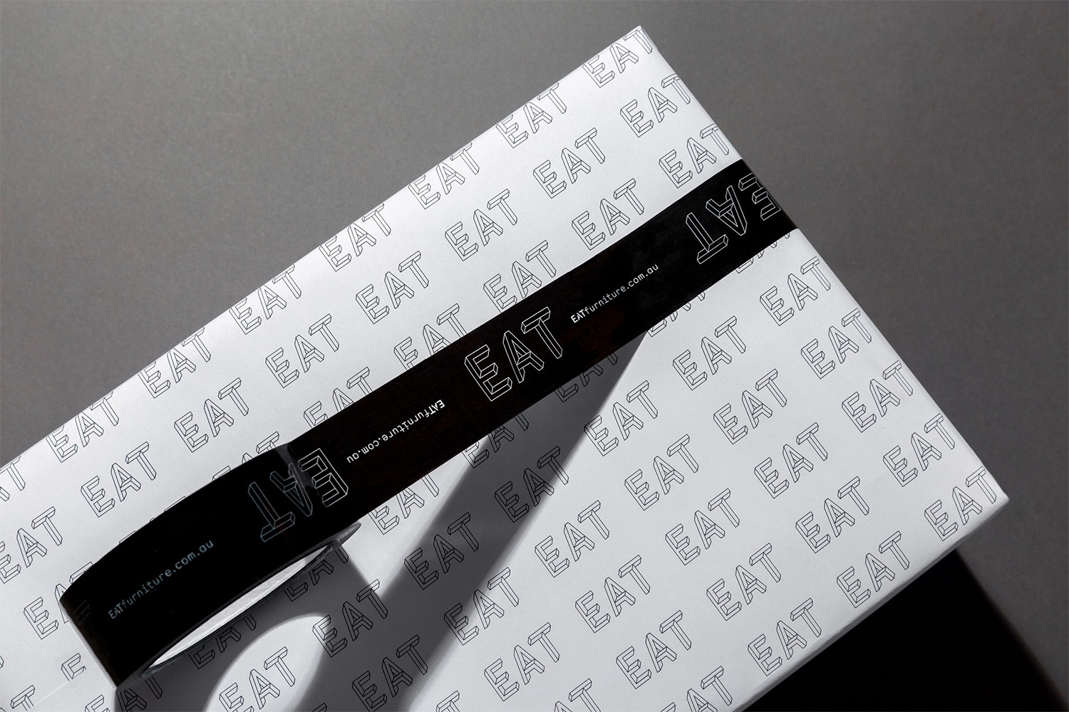 White packaging box with repeating Eat logo pattern sealed with glossy black branded tape on a dark surface.