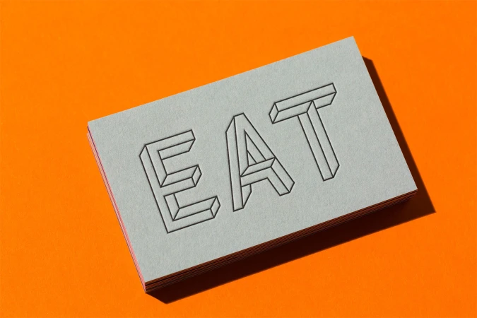 Stacked business cards with the word EAT embossed in block lettering resting on a textured orange background