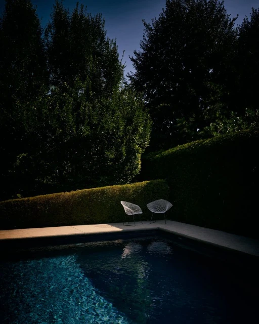 Tranquil scene of an outdoor swimming pool with two white chairs and lush greenery in the background, creating a serene and inviting atmosphere.