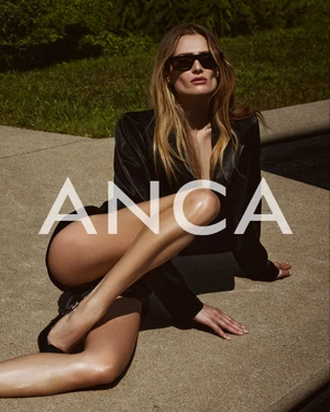 Model wearing dark sunglasses and a black blazer seated outdoors on a concrete ledge for the ANCA Spring Summer 2025 campaign.