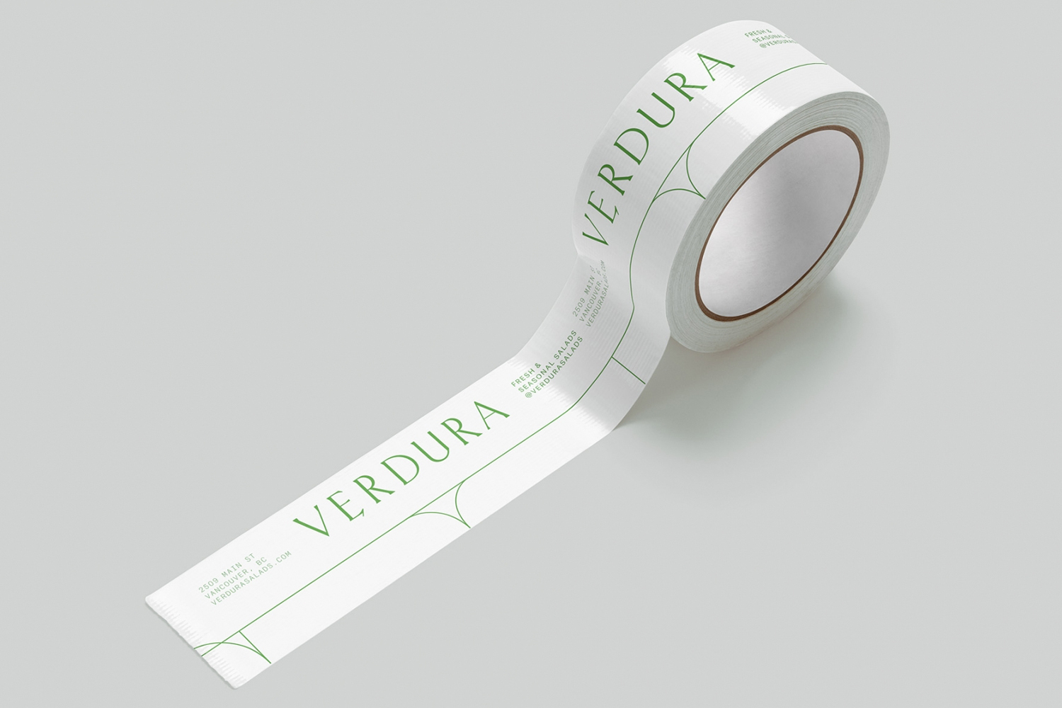 White branded packaging tape with green Verdura logotype unwinding across a seamless grey background