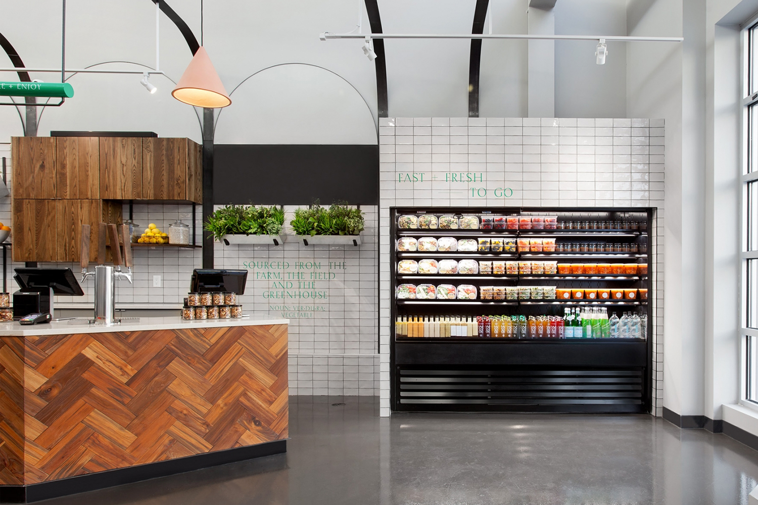 Modern retail interior featuring a herringbone wood counter, white tile walls, and a black refrigerated display case.
