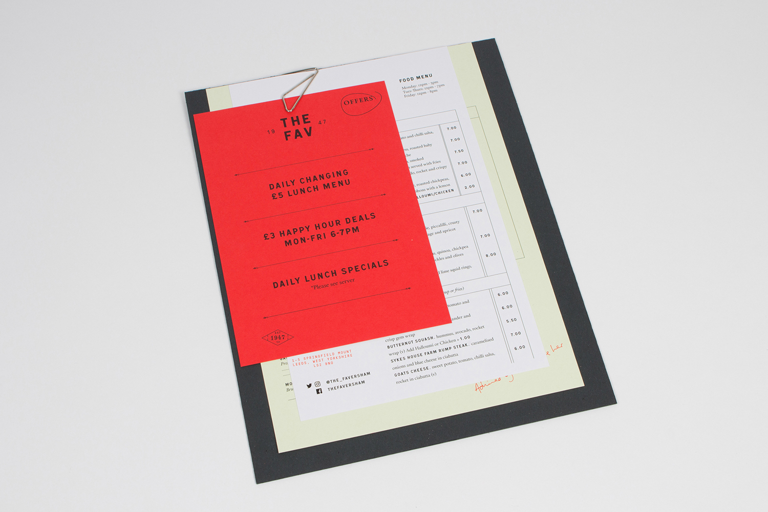 A red paper insert and white menu clipped to a dark backing board on a neutral white surface.