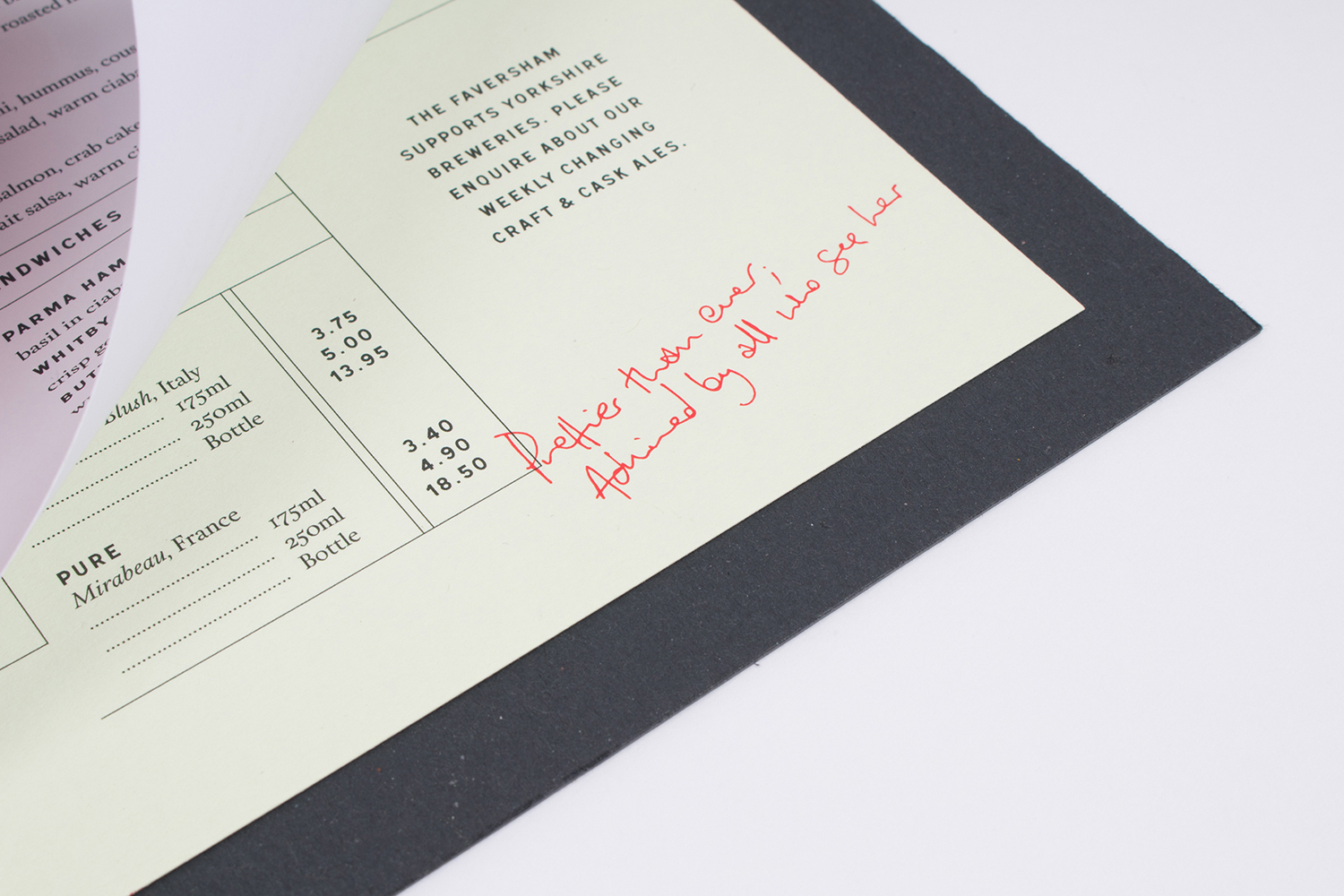 Close-up of a restaurant menu page with printed text, pricing columns, and handwritten red ink script on light paper