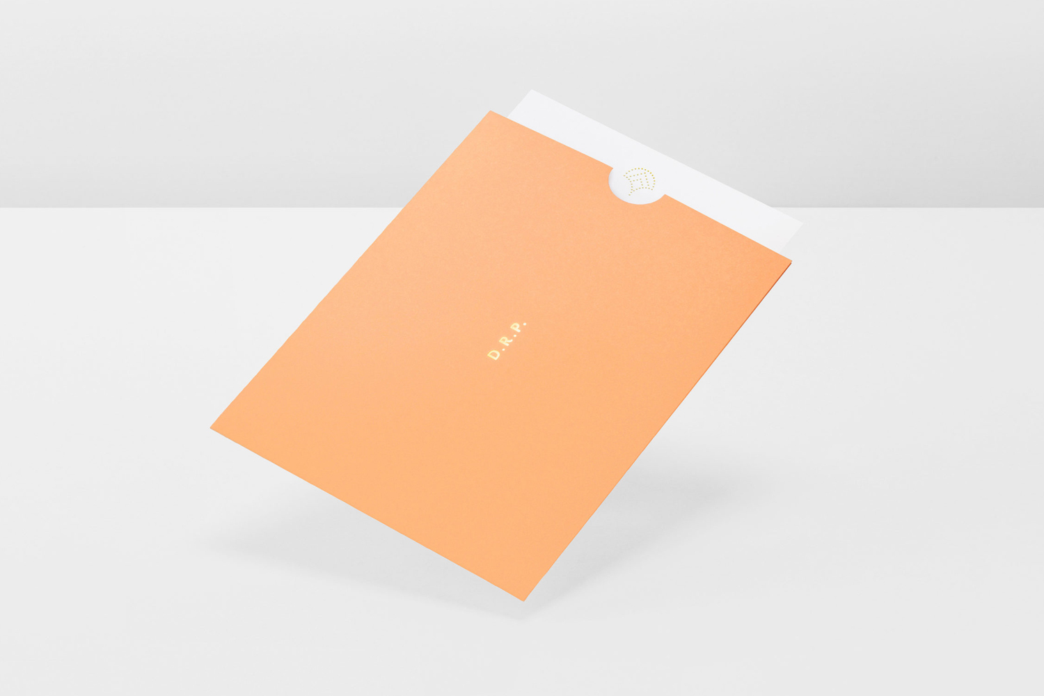Peach-colored envelope with gold foil lettering resting on a white studio surface