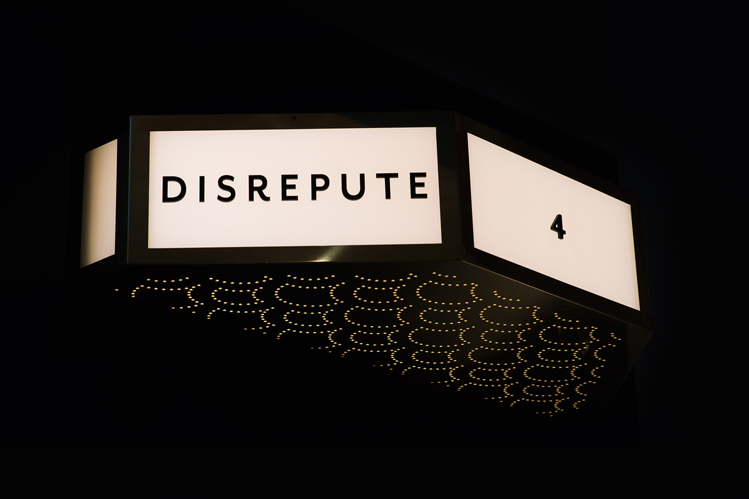 Illuminated storefront sign reading Disrepute with the number four against a dark night background