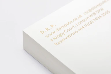 Close-up angled shot of a thick stack of white paper with gold foil stamped typography and text on a neutral surface.