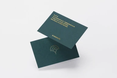 Two dark green business cards with gold foil lettering and logo displayed against a plain white background
