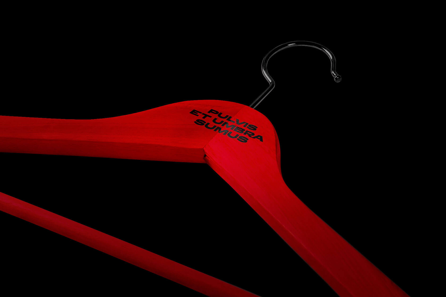Bright red wooden clothes hanger with black metal hook against a solid black background, featuring typography.