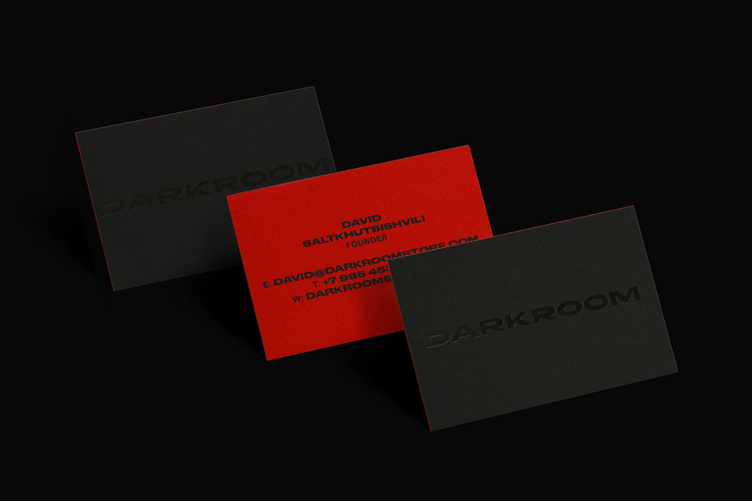 Three business cards for Darkroom featuring black embossed cards flanking a central bright red card with black typography on a black background.